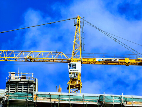 Construction crane lifts materials at a building site in Oahu under a blue sky during daytime