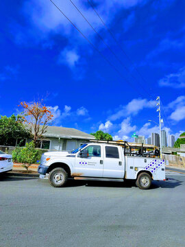 Hawaiian Electric truck parked on street with buildings in background and blue sky above