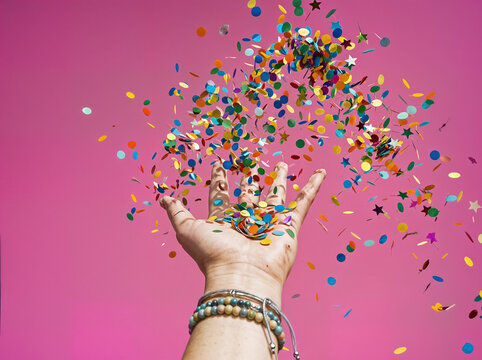 hand throwing colorful confetti on pink background