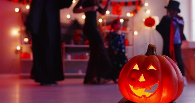 Halloween celebration and entertainment concept. Faceless parents and their children dancing together to music, have home party, celebrate their favourite holiday. Jack o lantern in foreground