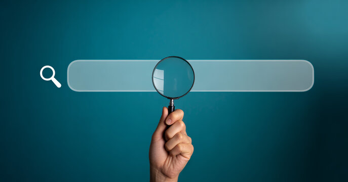 Hand holding magnifying glass over blank search engine bar on blue gradient background for information discovery.