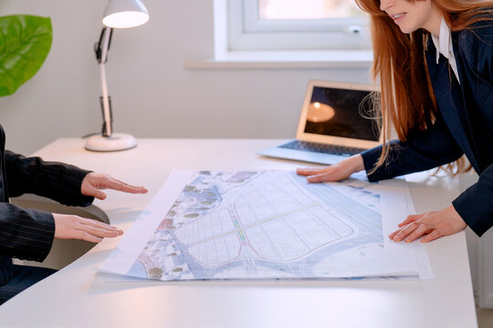 Meeting for project planning involves discussion over layout plans with a laptop on the desk in an office during daytime work hours 
