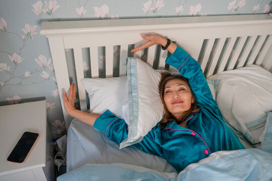 Woman wakes up and stretches in a cozy bedroom during morning hours on a weekday  