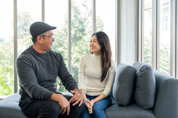 Obraz premium Happy Grandparents Asian family bonding at home. Smiling daughter hugs her elderly father. Dad and daughter on the sofa sharing laughter love and warmth in a joyful family