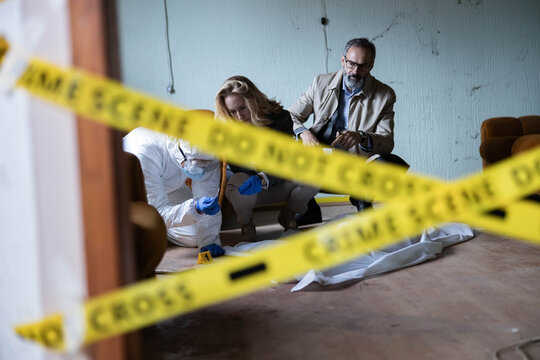 Forensic team and detective investigating a crime scene inside an old room, collecting evidence behind yellow police tape