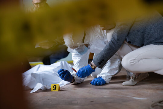 Forensics team members collecting samples and documenting the scene of a crime with a body under a sheet and an evidence marker