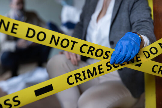 Detective examining evidence behind crime scene do not cross tape, focusing on forensic investigation and law enforcement