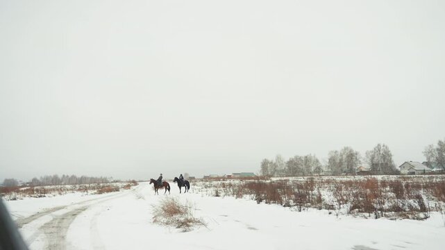 Distant riders crossing snowy road from vehicle, photographer viewpoint through car window, tiny figures on horizon, wide negative space, muted overcast sky, remote winter landscape, cinematic expanse