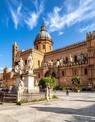 Fototapeta premium Large ornate cathedral with a prominent dome and intricate architecture stands against a blue sky, with statues in the foreground