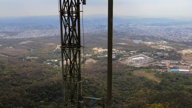 Aerial Lateral Slide Past Telecommunications Antenna Tower Over Mountain City Landscape 4K