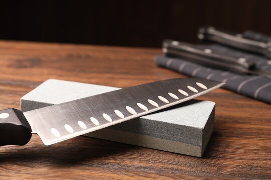 Sharpened knife and whetstone on wooden table. Space for text