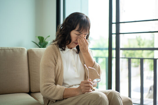 Unhappy asian senior woman feeling tired and exhausted while sitting on the sofa in the living room at home, elderly female retirement stressed with depression planning for healthcare life insurance