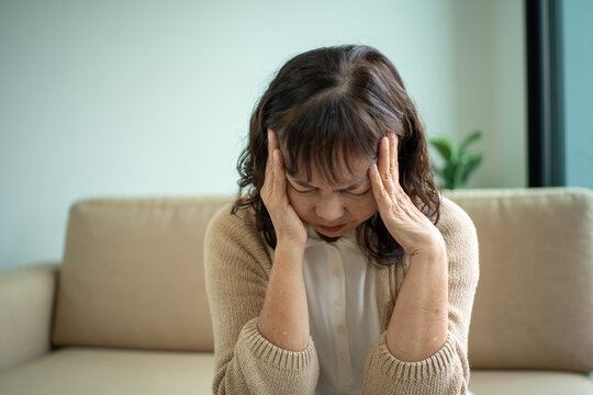 Unhappy asian senior woman feeling tired and exhausted while sitting on the sofa in the living room at home, elderly female retirement stressed with depression planning for healthcare life insurance