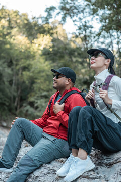 Couple Hiker man and woman climbing rocky mountain to explore cave hill and river enjoying outdoor adventure trekking, and nature travel. Two traveller and nature lover on an exciting hiking journey