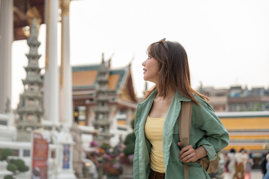Young woman solo traveling alone backpacker walking in temple at Bangkok Thailand. Happy female tourist walking in the downtown street traditional ancient temple. Holiday vacation time tourist