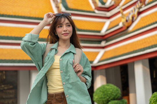 Young woman solo traveling alone backpacker walking in temple at Bangkok Thailand. Happy female tourist walking in the downtown street traditional ancient temple. Holiday vacation time tourist