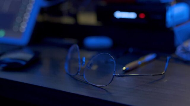 Lentes de productor sobre escritorio con paneo hacia estaci&oacute;n de trabajo de audio digital en estudio - 4K