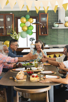 Host raising glass initiating toast, group clinking glasses, passing bread and sharing food