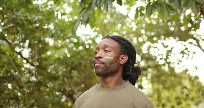 African man under leaves sun drawing gaze up responding to camera by turning and smiling facepaint