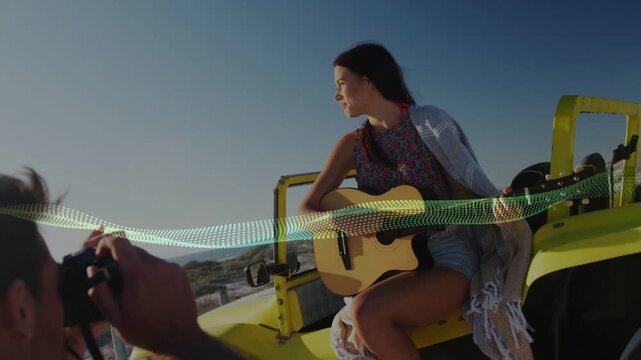 Man lifting camera, shooting woman with guitar on buggy for travel ads, waveform crossing frame