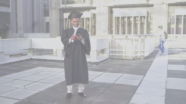 Male graduate ending call, smiling, raising phone to selfie with diploma and graduation on rooftop