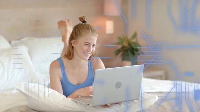 Woman typing on laptop in bed, generating animated circuit lines and blocks while doing tech design