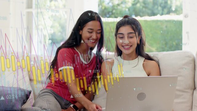 Two women sitting couch, left tapping trackpad, laptop charts animating highlighting finance review