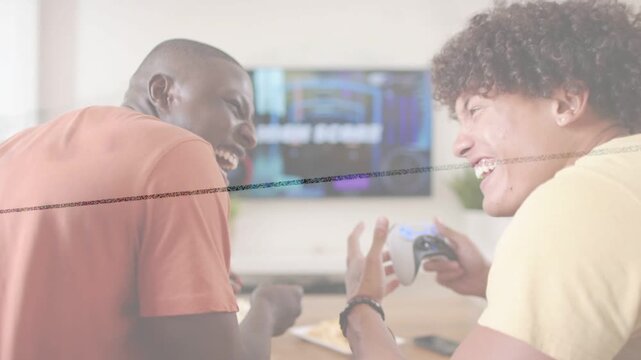 Two friends sitting at low table, right friend using controller sparking laughter during gaming