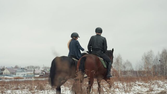 Two persons journeying through winter terrain. Two individuals traverse frostcovered open land scene. Two travelers move across chilled rural landscape with distant homes and leafless trees