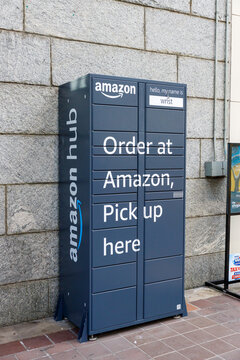 Navy-blue Amazon Hub parcel locker named Wrist, reading Order at Amazon, Pick up here, mounted against a stone block wall in downtown Vancouver.