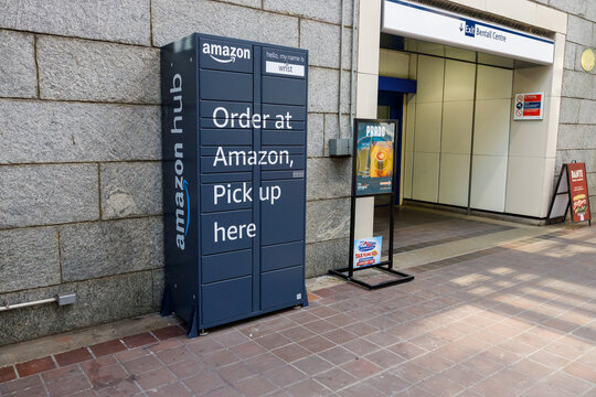 Navy-blue Amazon Hub parcel locker beside the Bentall Centre exit of Burrard SkyTrain Station, with poster ads and a sandwich board on a tiled walkway.