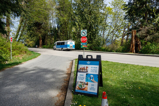 A blue Stanley Park shuttle bus drives past a Prospect Point cafe sandwich-board sign at the Prospect Point lookout in Stanley Park.