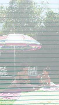 Vertical video: Two adults sitting under umbrella, camera pulling back revealing lawn for brands