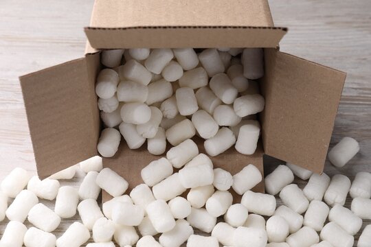 Cardboard box with styrofoam pieces on wooden background, closeup