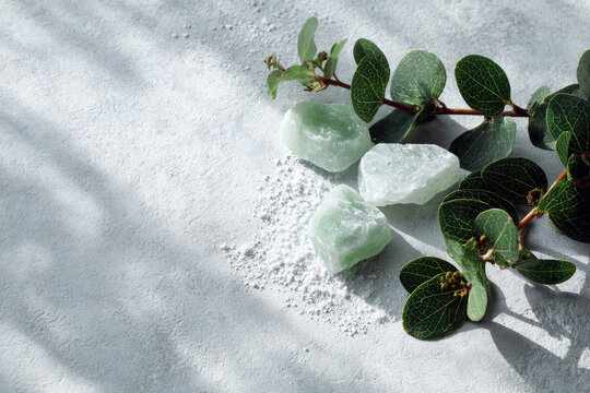 Salt stones and green Leaves of riskus in the sun, with shadows, on a white gray concrete background with copy space. Advertising background concept for cosmetics, fashion, spa. Banner 