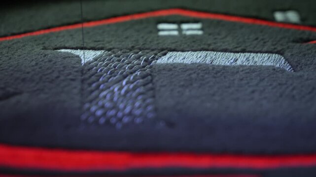 Machine embroidery on a black fleece blouse with red and grey thread. House roof embroidery. Selective focus close-up.