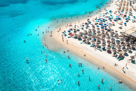 Aerial view of colorful umbrellas on white sandy beach, swimming people in blue sea on sunny summer day. Sardinia, Italy. Tropical landscape with clear azure water. Summer travel. Top view of ocean
