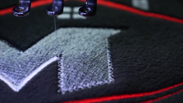 Machine embroidery on a black fleece blouse with red and grey thread. House roof embroidery. Selective focus close-up.