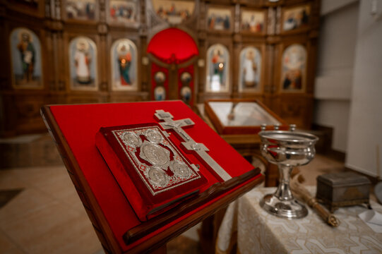 Orthodox Gospel book and silver cross on red velvet lectern in church with iconostasis background