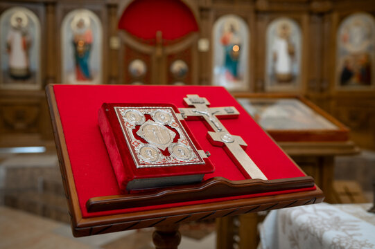Orthodox Gospel book and silver cross on red lectern in church with blurred iconostasis background