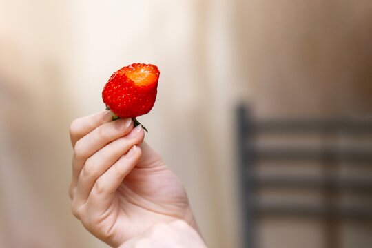 Young woman's hand holding a bitten ripe strawberry, showing the fresh juicy inside.