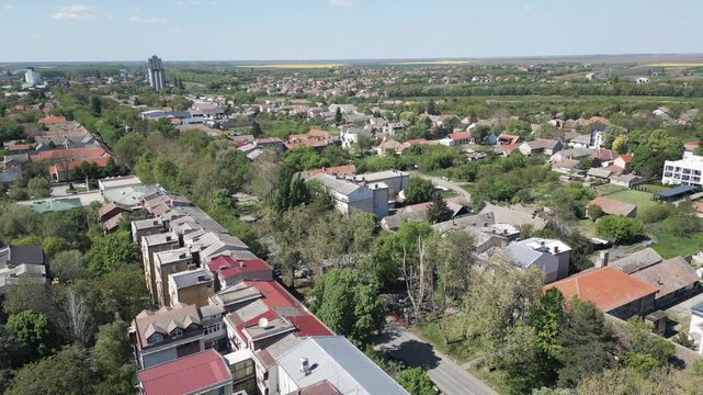 Cinematic aerial ascending shot from Vrbas city center, northern Serbia. Drone rises to reveal a wide panorama of the town and vast Vojvodina plains under a bright sunny sky.