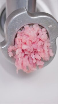 Grinding raw beef and pork for cooking. Home cook uses electric grinder to prepare minced meat. Closeup of manual meat mincing for burgers and sausages on kitchen counter