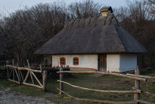 Traditional Ukrainian khata with thatched roof behind a rustic wooden fence 