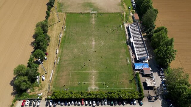 Aerial View of a Rural Football Field: An expansive aerial shot showcases a verdant football pitch nestled amidst agricultural fields, bordered by trees and a modest grandstand.