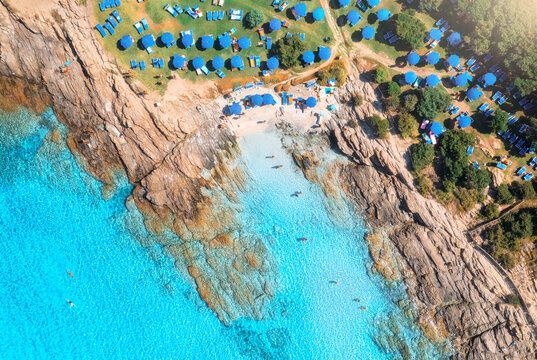 Aerial drone view of sea bay, sandy beach with umbrellas, stones and rocks in water at sunset in summer. Sardinia, Italy. Tropical scenery with sea lagoon, swimming people, blue water. Top down view