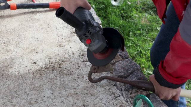 Worker using an angle grinder for sharpening a metal hoe blade creating sparks. Man with a power tool preparing a gardening instrument for working in the yard