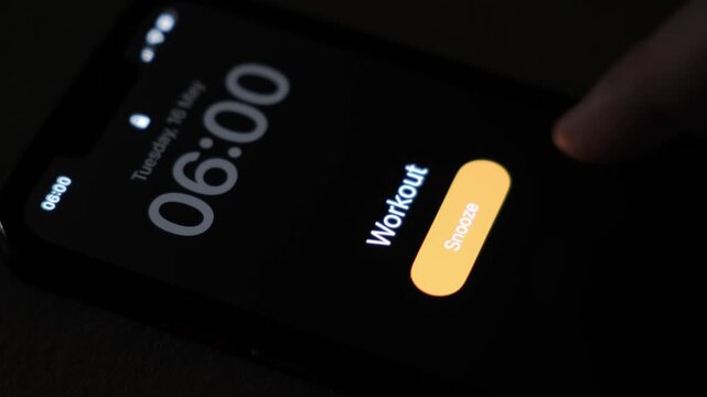 A smartphone alarm rings at 6 AM with the workout label on a dark screen showing a snooze button and an early wake up moment before morning exercise. High quality 4k footage