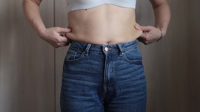 The girl does not fit into jeans, excess weight and sides on the stomach, slight obesity, the concept of weight loss.