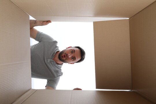 Man looking into cardboard box on white background, view from inside package